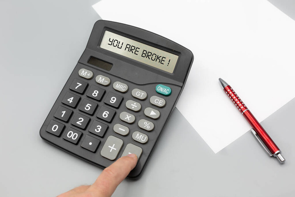 Человек зарядил калькулятор активами и деньгами и получает указание на то, что он на мели. Горизонтальная с ручкой и бумагой - Фото, изображение