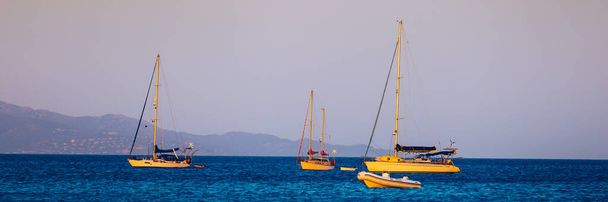 Yacht αγκυροβόληση σε κρυστάλλινα γαλαζοπράσινα νερά μπροστά από το τροπικό νησί, εναλλακτικό τρόπο ζωής, που ζουν σε ένα σκάφος. Αεροφωτογραφία του γιοτ αγκυροβολημένο σε γαλαζοπράσινα νερά, που δείχνει πολυτέλεια, πλούτο. - Φωτογραφία, εικόνα