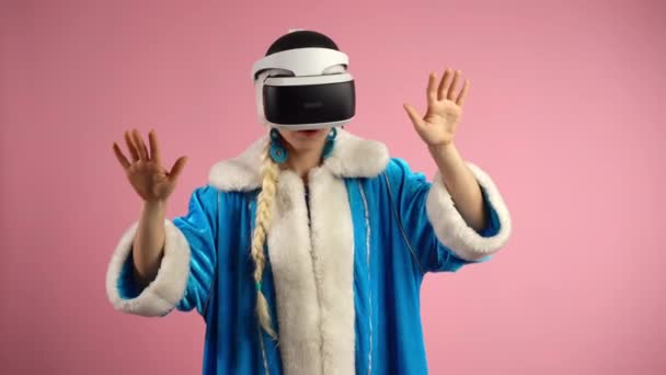 Testing virtual reality glasses on isolated pink background, excited woman in christmas clothes playing 3D virtual video game, moving her body in space and gesturing with hands. Interactive games in - Video