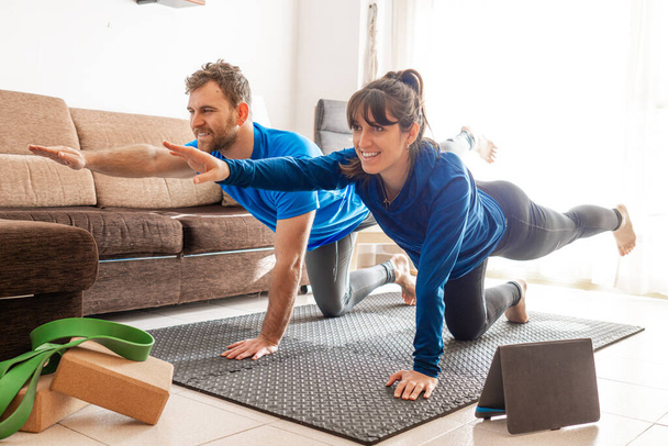 Casal de exercício na sala de estar seguinte vídeo de tablet, mulher e homem esticado em tapete de exercício com tablet e blocos de ioga. - Foto, Imagem