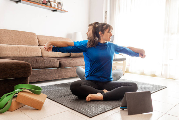 couple practicing yoga in the living room back to back and arms outstretched, they follow routine from the tablet - Photo, Image