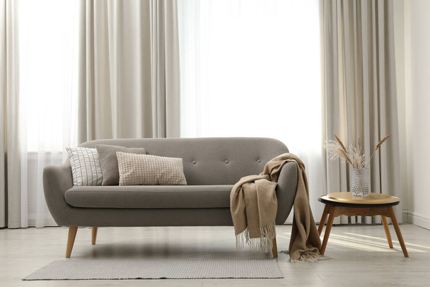 Grey sofa with pillows near window in stylish living room interior - Фото, изображение
