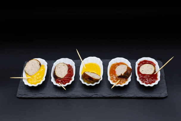 small try-out plates with bratwurst, currywurst and other sausages plus various sauces and dips. Plates in a row with black background - Photo, Image