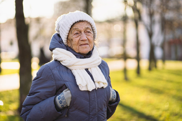 Retrato al aire libre de la mujer mayor en chaqueta, bufanda y desgaste de la cabeza en invierno. Feliz jubilación. Alegre anciano posando en el parque, tiempo frío soleado. Mujer madura feliz disfrutando de caminar en la ciudad. - Foto, imagen