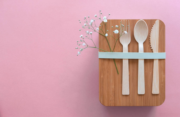 Set of cutlery (fork, spoon, knife) made of wood or bamboo, bamboo reusable lunch box. Zero waste concept. Pink background. Top view.  - Foto, imagen