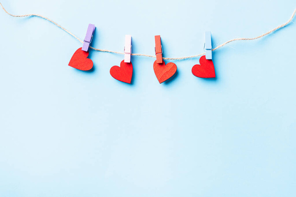 Valentýnský koncept. červená srdce ve tvaru valentines dekorace visí s dřevěné spony pro šťastnou lásku na laně blahopřání izolované na modrém pozadí s kopírovacím prostorem - Fotografie, Obrázek