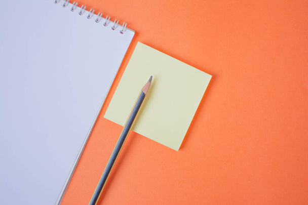 Μολύβι και σημειωματάριο σε πορτοκαλί φόντο - Φωτογραφία, εικόνα
