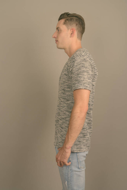 Νεαρός όμορφος άντρας με γκρι πουκάμισο σε γκρι φόντο - Φωτογραφία, εικόνα