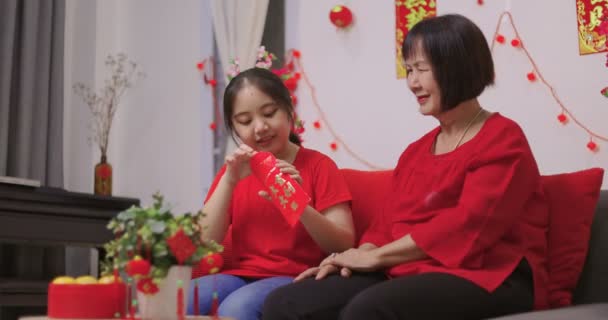 Χαρούμενη ηλικιωμένη Ασιάτισσα που δίνει στην εγγονή της ένα τυχερό κόκκινο φάκελο για το κινέζικο δώρο της Πρωτοχρονιάς. - Πλάνα, βίντεο