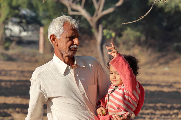 Egy gyönyörű indiai kisgyereket kézzel vágnak le, és az indiai nagyapát látják a kertben nyírni, Indiában. - Fotó, kép