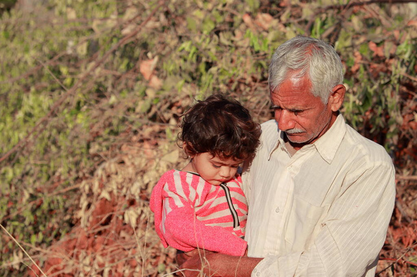 Hintli küçük bir çocuk büyükbabasının kucağında oturuyor ve Hindistan 'da doğanın tadını çıkarıyor. - Fotoğraf, Görsel