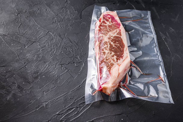 Góra ostrze stek, pakowane próżniowo wołowiny organiczne do gotowania sous vide na czarnym tle teksturowane, widok z boku z miejsca na tekst - Zdjęcie, obraz