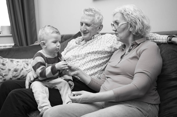 Großeltern mit ihrem kleinen Enkelkind, das zu Hause ruht - Foto, Bild