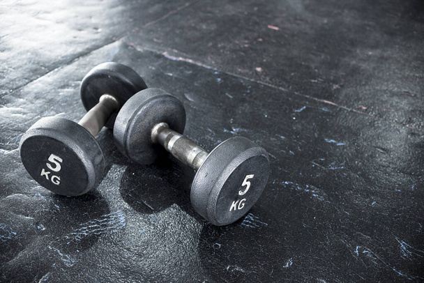 A pair of dumbbells of moderate weight lying on worn black rubber floor panels at a gym or fitness center. - Photo, image
