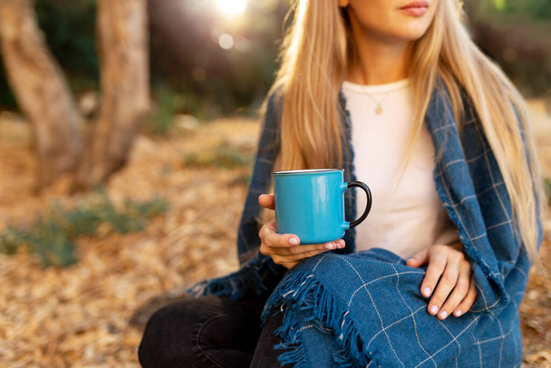 Holding cup of coffe in autumn season, cozy unrecognizable female holding autumn tea, covered with blue warm plaid - Foto, imagen