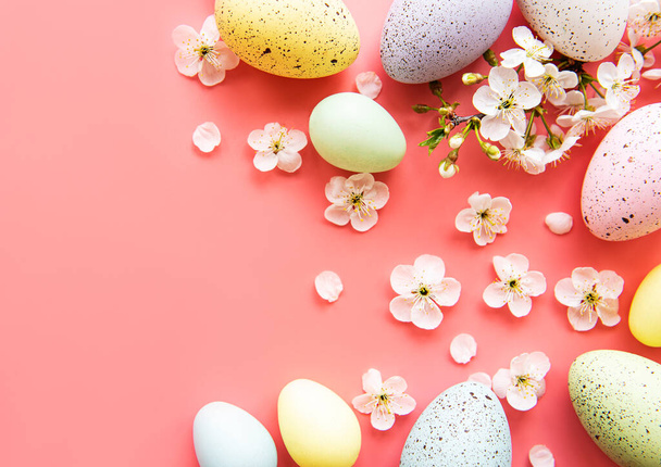 Színes húsvéti tojás tavaszi virágokkal rózsaszín háttér felett. Színes tojás Nyaralási határ.  - Fotó, kép