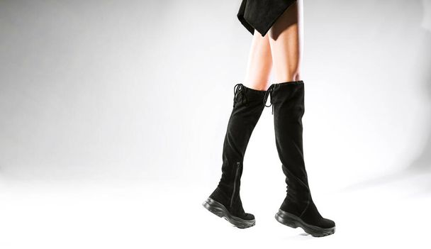 las piernas de la muchacha en las botas a la moda negras sobre el fondo blanco en el estudio. botas de moda con estilo otoño invierno - Foto, Imagen