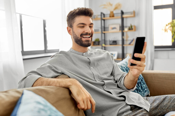 happy smiling young man with smartphone at home - Фото, изображение