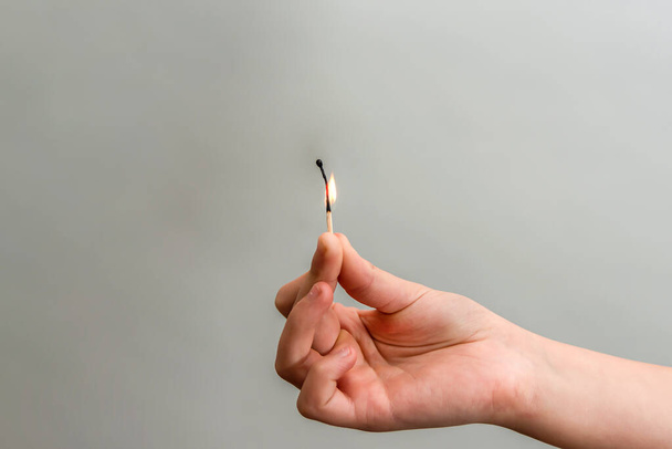 The girl holds a nearly burnt match with her hand on a gray background. - Photo, Image
