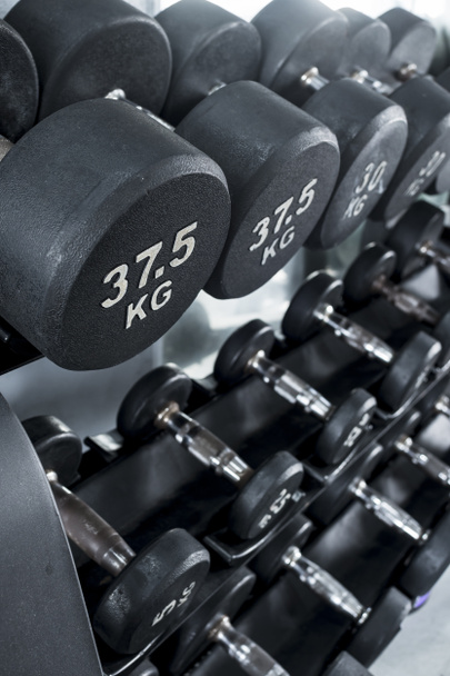 Különböző súlyú gumival bevont súlyzók vannak az edzőteremben. Súlyzós gyakorló berendezés. - Fotó, kép