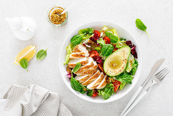 Grilled chicken meat and fresh vegetable salad of tomato, avocado, lettuce and spinach. Healthy and detox food concept. Ketogenic diet. Buddha bowl dish on white background, top view - Φωτογραφία, εικόνα