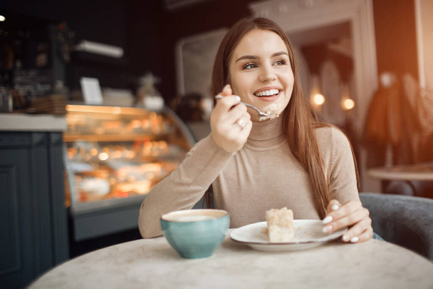 Boldog csinos nő a kávézóban egy csésze kávéval és tortával. - Fotó, kép