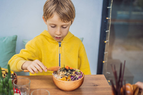 Мальчик ест сырую органическую миску с рисом и овощами крупным планом на столе. Вид сверху горизонтальный - Фото, изображение