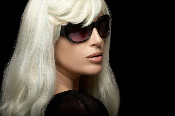Modeporträt einer attraktiven blonden Frau mit gesunden langen silberweißen Haaren, die eine schwarze Sonnenbrille trägt und über die Schulter blickt. Nahaufnahme isoliert auf schwarzem Hintergrund mit Kopierraum für Text - Foto, Bild