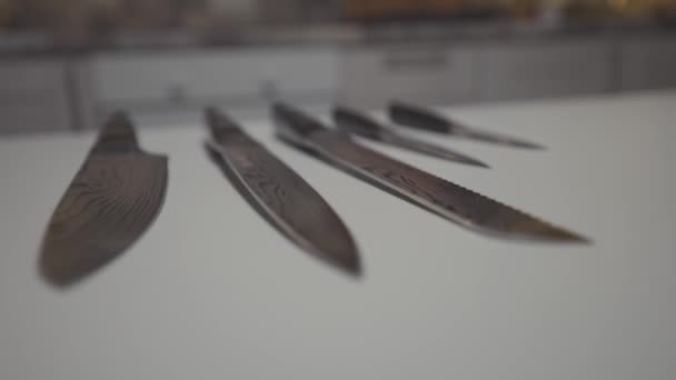 Close up de facas conjunto deitado sobre uma superfície de mesa branca na cozinha. Acção. Novas facas de aço afiadas, conceito de cozinhar.  - Filmagem, Vídeo