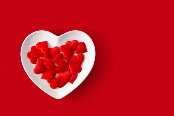 Hartvormige plaat met rode hartjes binnen op rode achtergrond - Foto, afbeelding