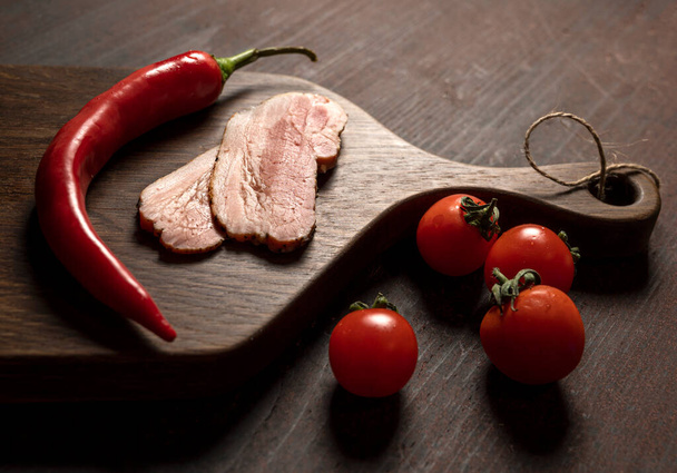 Slices of bacon, tomatoes, pepper on a wooden board on the table  - Fotó, kép