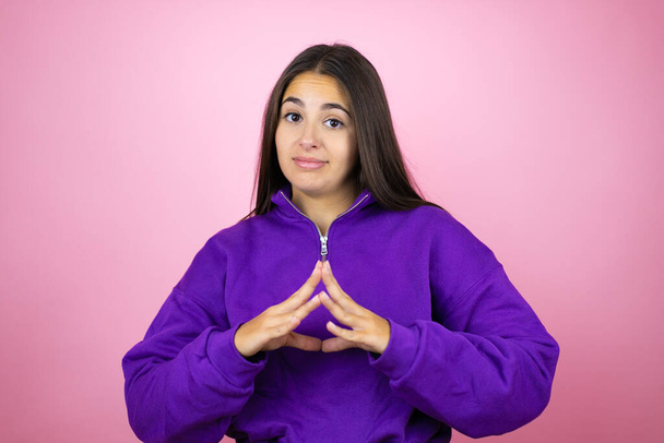 Jonge mooie vrouw draagt sweatshirt over geïsoleerde roze achtergrond met handen bij elkaar en vingers gekruist lachend ontspannen en vrolijk. Succes en optimisme - Foto, afbeelding