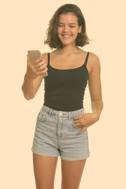 Young happy Caucasian teenage girl smiling and holding mobile phone - Zdjęcie, obraz