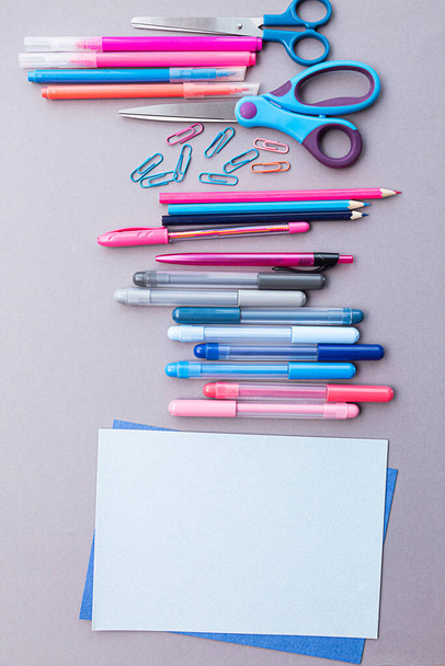 Diverse briefpapier in roze en blauwe kleuren, blanco vellen papier, op een grijze achtergrond met kopieerruimte. Plat gelegd met potloden, scharen, pennen, paperclips, viltstiften en vellen papier. - Foto, afbeelding