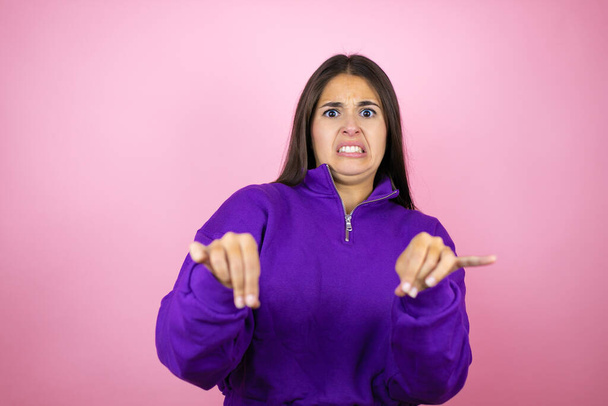 Junge schöne Frau trägt Sweatshirt über isoliertem rosa Hintergrund angeekelten Ausdruck, unzufrieden und ängstlich dabei Ekel Gesicht, weil Abneigung Reaktion. Ärgerliches Konzept - Foto, Bild