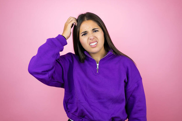 Jonge mooie vrouw draagt sweatshirt over geïsoleerde roze achtergrond verwarren en vragen zich af over de vraag. Onzeker met twijfel, denken met de hand op het hoofd - Foto, afbeelding