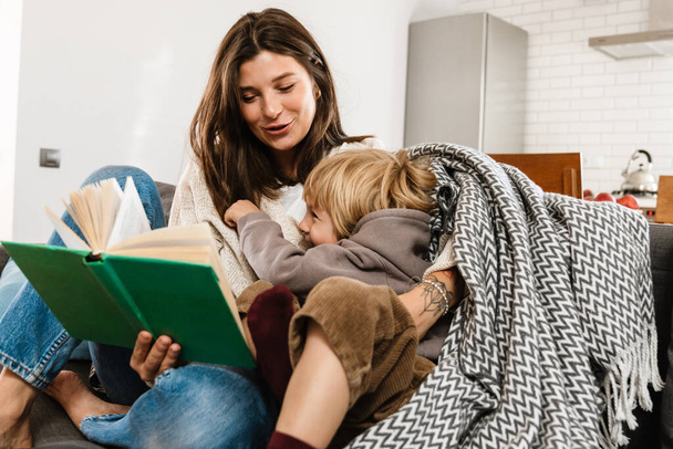 Image of young pretty woman reading a book at home for her son - Foto, imagen