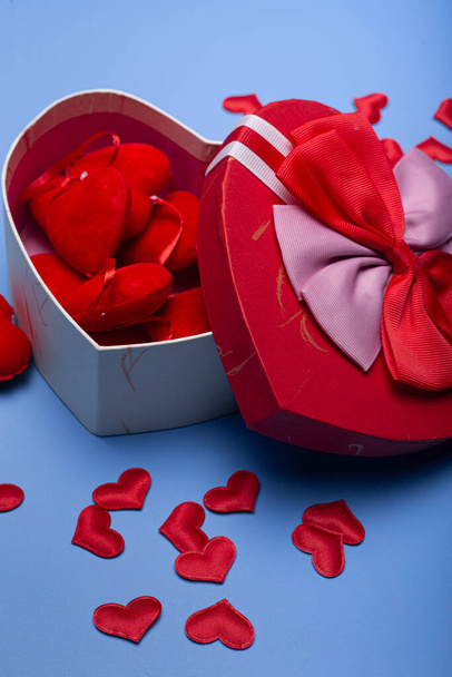 Immagine isolata di una scatola a forma di cuore piena di cuori su uno sfondo blu. Buon San Valentino. Quadro verticale - Foto, immagini
