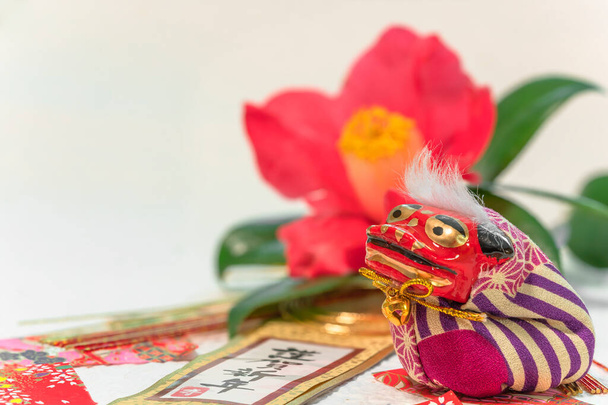 Tarjeta de Año Nuevo Japonés con un primer plano en una figura de leones Shishi contra una flor de camelia tsubaki y una las palabras Kingashinnen que significa Feliz Año Nuevo. - Foto, Imagen