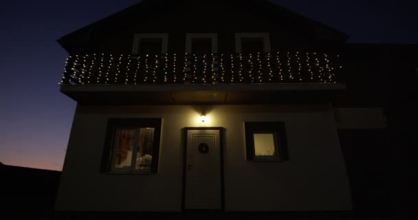 Amplo Estabelecimento Tiro de uma casa à noite com fachada branca e marrom com varanda em um segundo andar e luzes de Natal - Filmagem, Vídeo