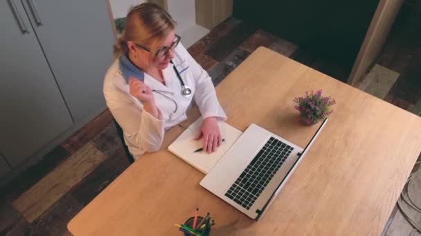 Βίντεο ανώτερης προβολής ενός ανώτερου γιατρού που έχει online διαβούλευση με έναν ασθενή χρησιμοποιώντας ένα φορητό υπολογιστή - Πλάνα, βίντεο