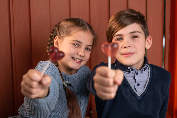Junge und Mädchen, die mit Heliumballons süße Bonbons in Herzform bringen, lachen. Konzept zum Valentinstag, 14. Februar, Selektiver Fokus - Foto, Bild