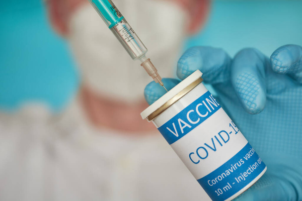 Badacz z maską do twarzy wypełnia strzykawkę szczepionką. Zbliżenie badacza z maską do twarzy napełniającego strzykawkę szczepionką przeciw koronawirusowi. - Zdjęcie, obraz