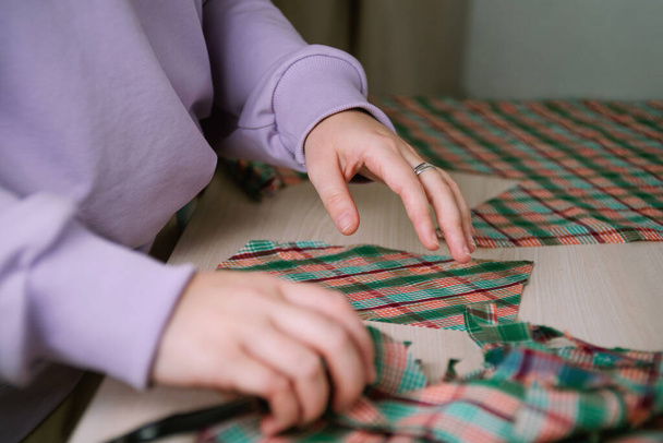 Closeup of female tailor cuting out checkered fabric with a paper pattern to make out a shirt - Φωτογραφία, εικόνα