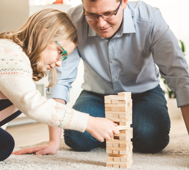 Happy young father playing with his cute daughter with wooden blocks at home - 写真・画像
