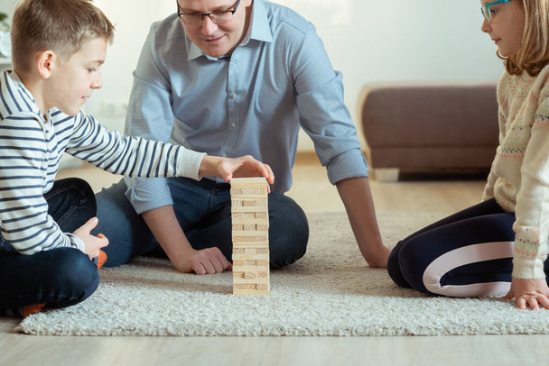 Young happy father playing with his two cute children with wooden blocks at home - Foto, Bild