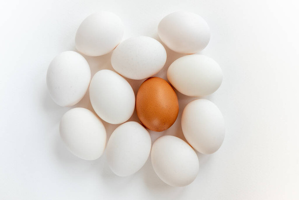 Μια ομάδα φρέσκων αυγών. Λευκά αυγά κοτόπουλου και ένα καφέ, απομονωμένο σε λευκό φόντο. Προετοιμασία για το βάψιμο πασχαλινών αυγών. Άνω όψη - Φωτογραφία, εικόνα