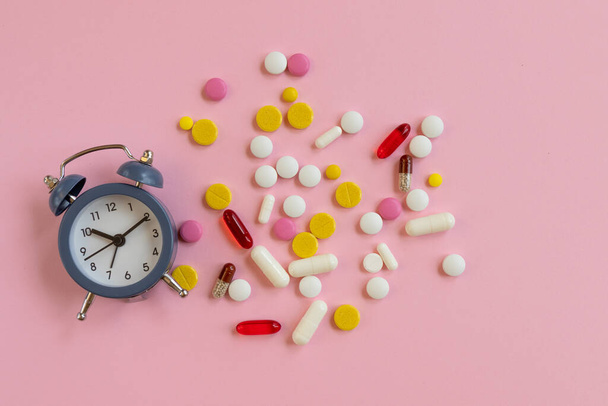 Muchas píldoras diferentes con despertador sobre un fondo rosa. Hora de tomar la medicina. vista superior - Foto, Imagen