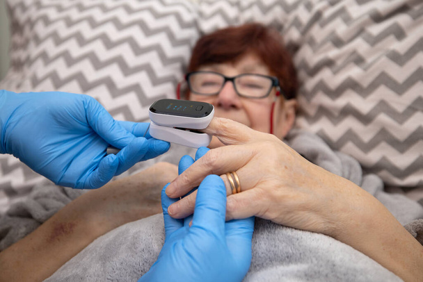 老人ホームでのCovid 19肺炎予防のための酸素濃度計検査高齢者,医師は自宅で酸素濃度計を使用して高齢女性を調べる - 写真・画像