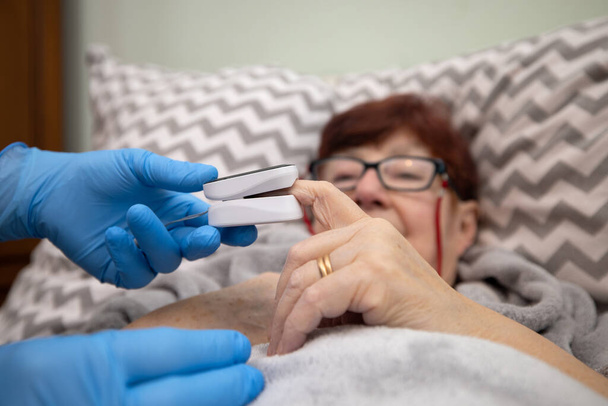 Oksimetritesti vanhuspotilas Covid 19 keuhkokuumeen ehkäisyssä hoitokodissa, lääkäri tutkii vanhempi nainen käyttää oksimetriä kotona - Valokuva, kuva